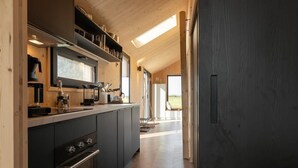 Une cuisine moderne équipée d’un four encastré, d’un four à micro-ondes et d’une machine à café. Une fenêtre se trouve au-dessus de l’évier, et une porte donne accès à un espace extérieur.