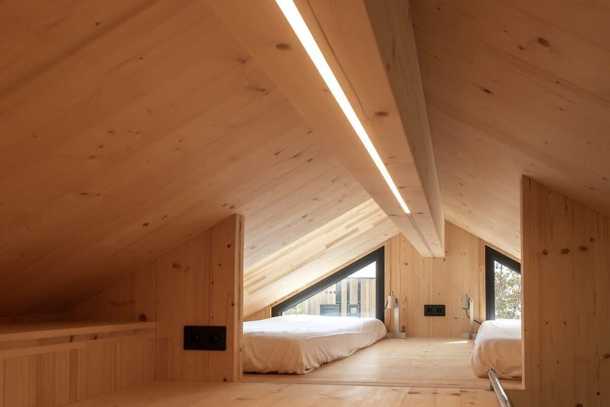 A wooden interior with a sloped ceiling, two beds, and a window.