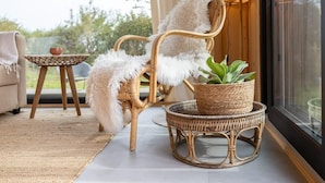 A wicker chair with a fluffy white cushion, a wicker table with a bowl, and a wicker basket with a plant. - Cosy tiny house for two in Westkapelle | Zeeuwse Liefde – Tiny House 3 (Westkapelle)