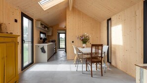 A modern kitchen with wooden walls, a dining area with a table and chairs, and a yellow cabinet. - Cosy tiny house for two in Westkapelle | Zeeuwse Liefde – Tiny House 3 (Westkapelle)