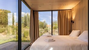 Ein modernes Schlafzimmer mit einem großen Bett, Holzboden und Blick ins Freie.