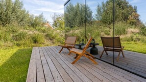 Eine Holzterrasse mit zwei Stühlen und einem Tisch, umgeben von viel Grün und Bäumen.