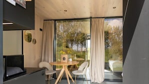 Ein modernes Zimmer mit einem runden Tisch, zwei Stühlen, einer Couch und einem großen Fenster mit Vorhängen.