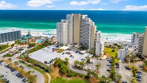A coastal hotel with multiple high-rise buildings, a parking lot, and a beach in the background.