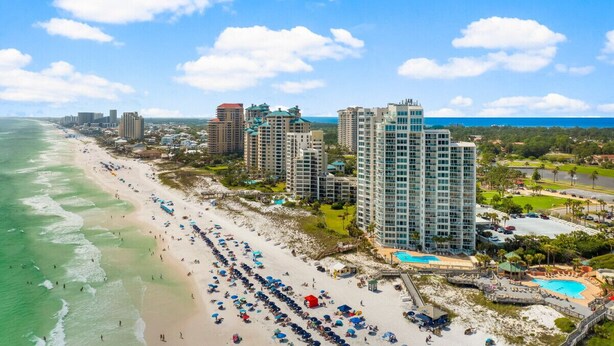 A coastal hotel with multiple high-rise buildings, a beach with umbrellas, and a swimming pool.
