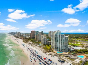 A coastal hotel with multiple high-rise buildings, a beach with umbrellas, and a swimming pool.