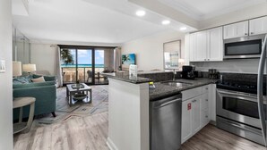 A modern kitchen with stainless steel appliances, a dining area with a view of the beach, and a living room with a large window overlooking the ocean.