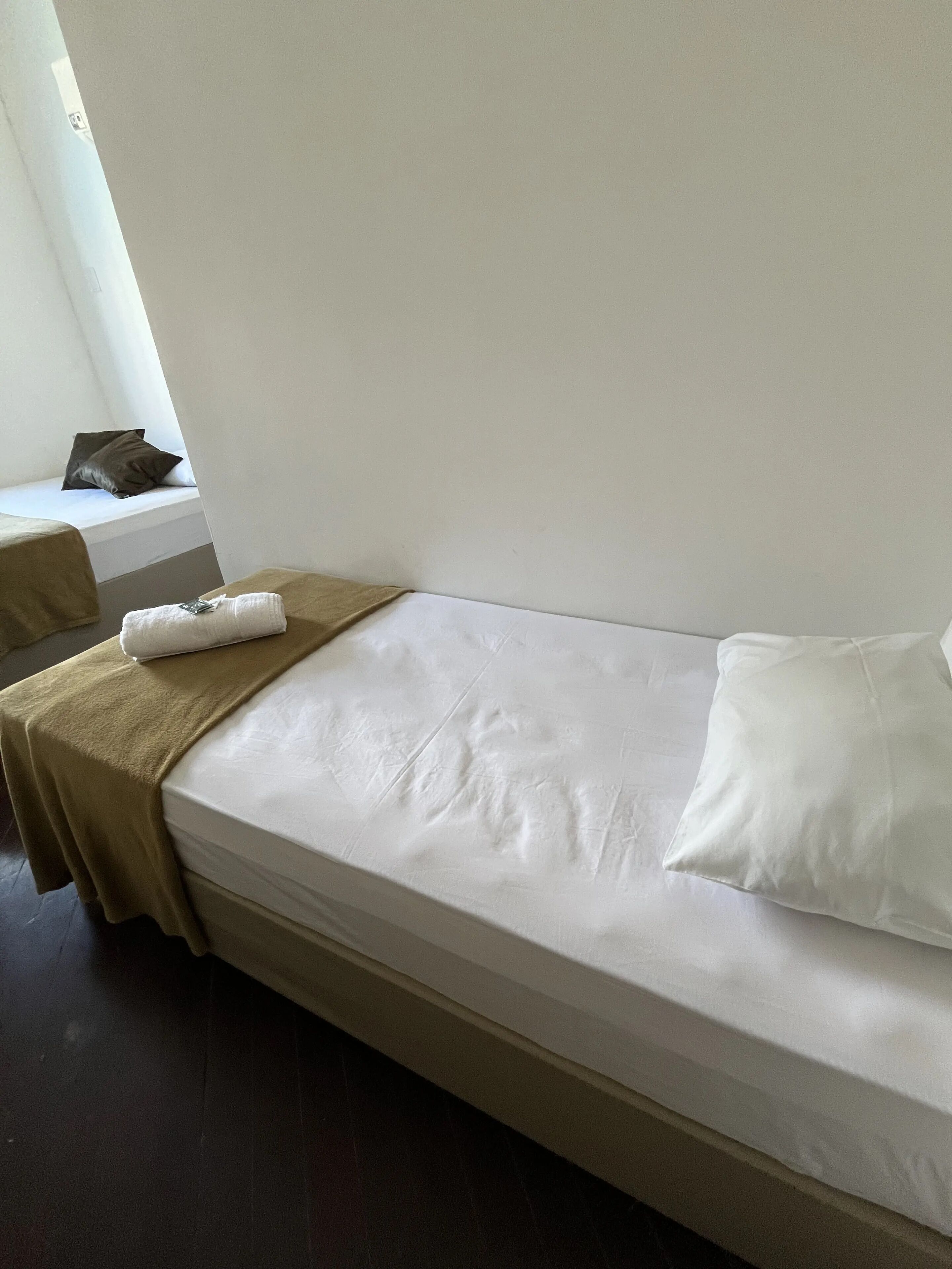 A single bed with a white mattress and a brown headboard, a white pillow, and a brown blanket.