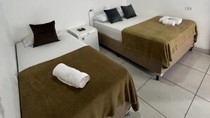 A hotel room with two beds, each with a brown blanket and a rolled towel. There is a ceiling fan, an air conditioning unit, and a small bedside table with a lamp. - Pousada Aloha Santos (Santos)
