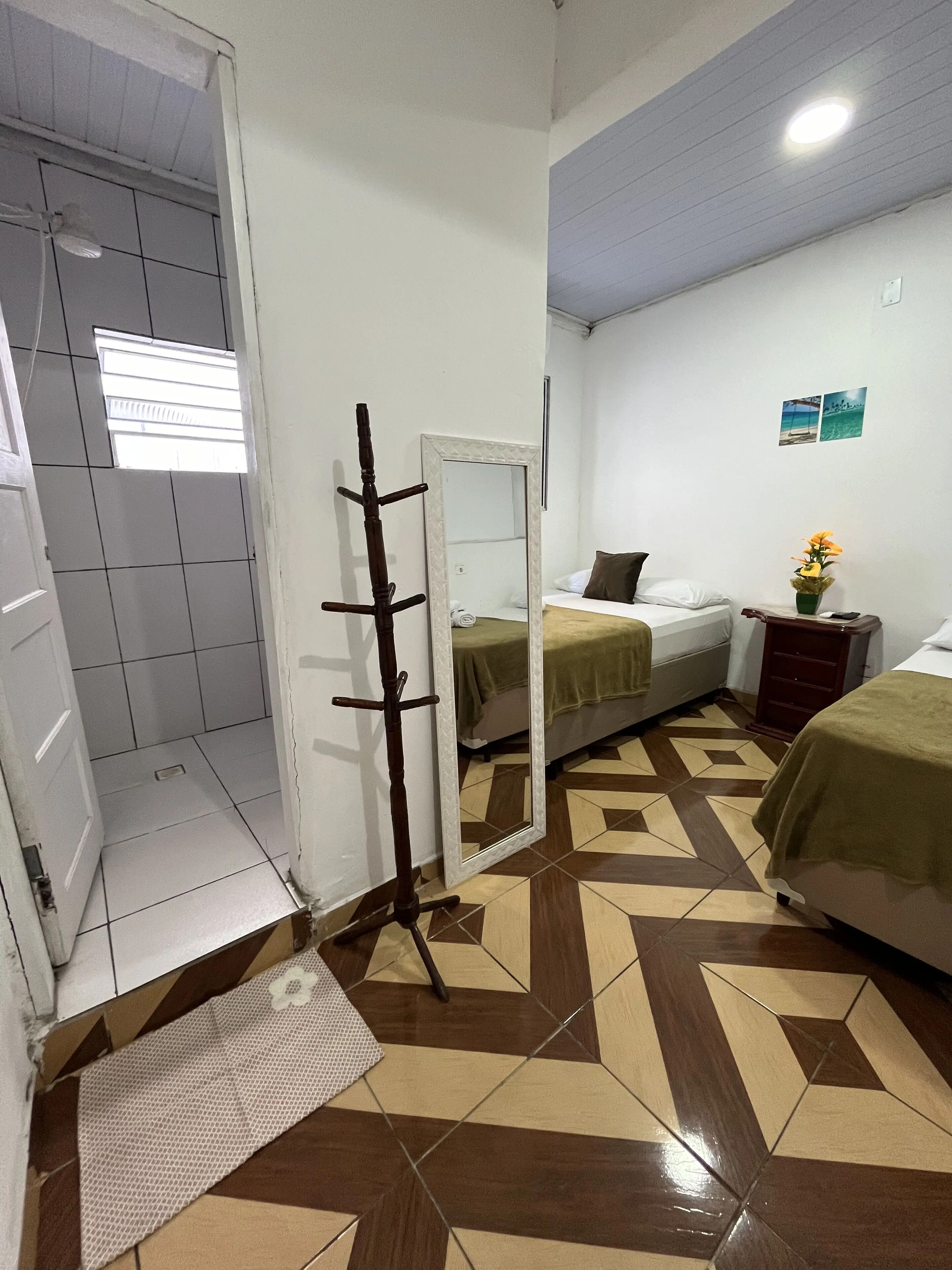 Habitación de hotel con cama, mesita de noche con un jarrón de flores, un espejo y zona de ducha.