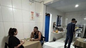A dining area with tables and chairs, a kitchen area with appliances, and a blue door. - Pousada Aloha Santos (Santos)