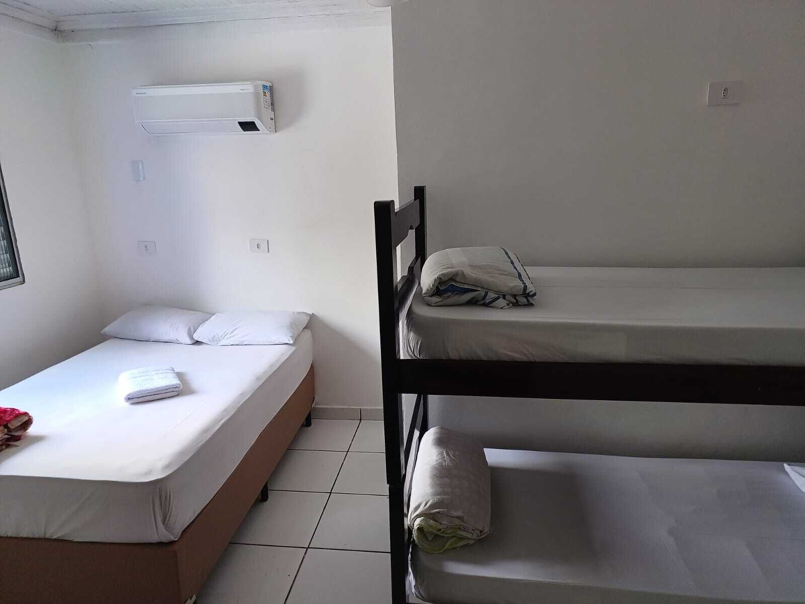 Quarto tipo dormitório com uma cama de solteiro, uma beliche e um aparelho de ar condicionado na parede.