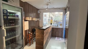 A small, well-lit room with a refrigerator stocked with beverages, a wooden counter, and a view of the street through a window. - Pousada Aloha Santos (Santos)