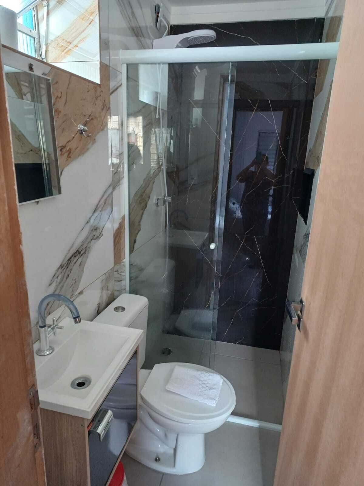 A modern bathroom with a glass-enclosed shower, a white toilet, and a sink with a marble backsplash.