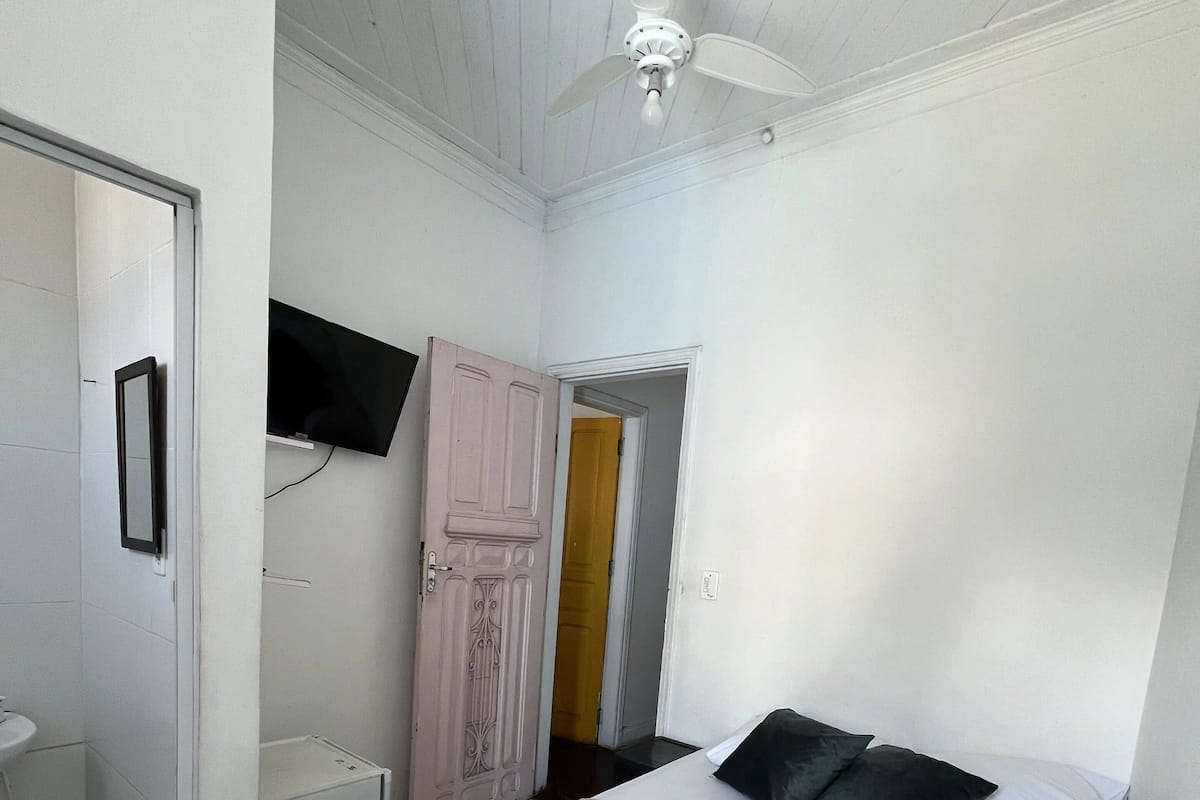 Un dormitorio con cama, almohadas, televisor montado en la pared y ventilador de techo.