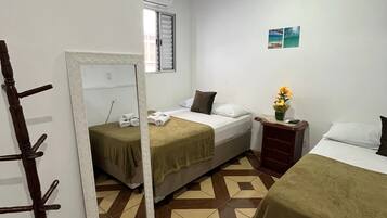 A hotel room with two beds, a mirror, a wooden chair, a small table with a vase, and a tiled floor.