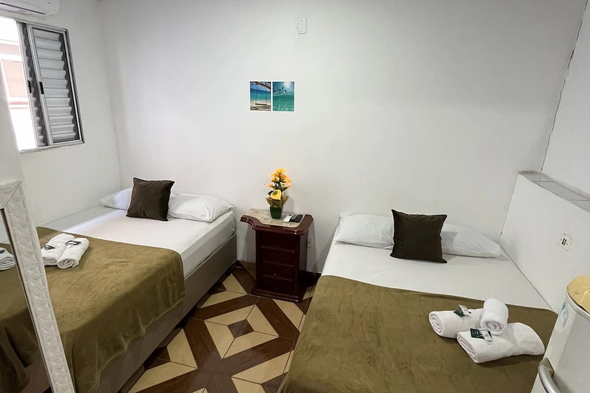 Una habitación de hotel con dos camas, una mesita con un florero y un espejo.