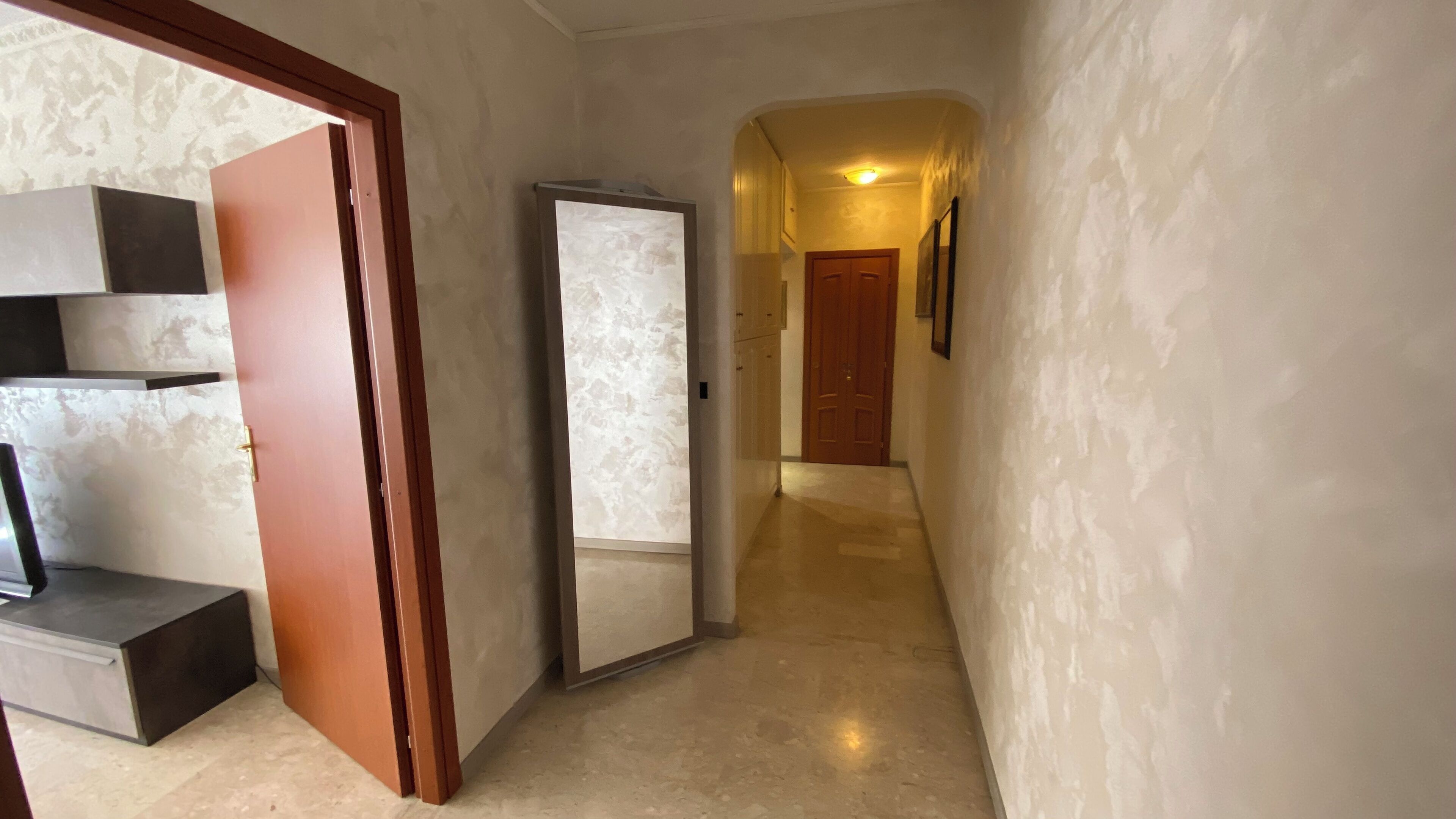 A hallway with a wooden door, a white wall, and a mirror.