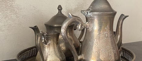 A set of silver tea service on a tray, including a teapot, a sugar bowl, and a creamer, placed on a dark surface against a light wall.