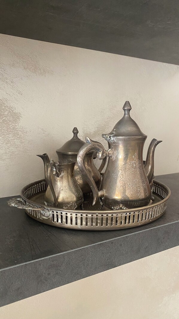 A set of silver tea service on a tray, including a teapot, a sugar bowl, and a creamer, placed on a dark surface against a light wall.
