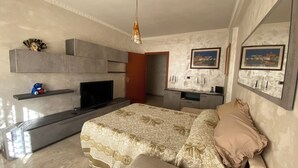 Une chambre moderne avec un téléviseur à écran plat, un lit avec une literie à motifs, une petite étagère avec un jouet et une porte donnant sur une autre pièce.