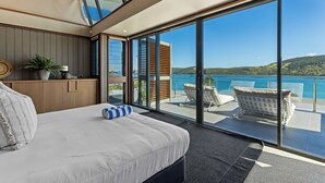 A modern hotel room with a large bed, a view of the sea, and a balcony with outdoor seating.