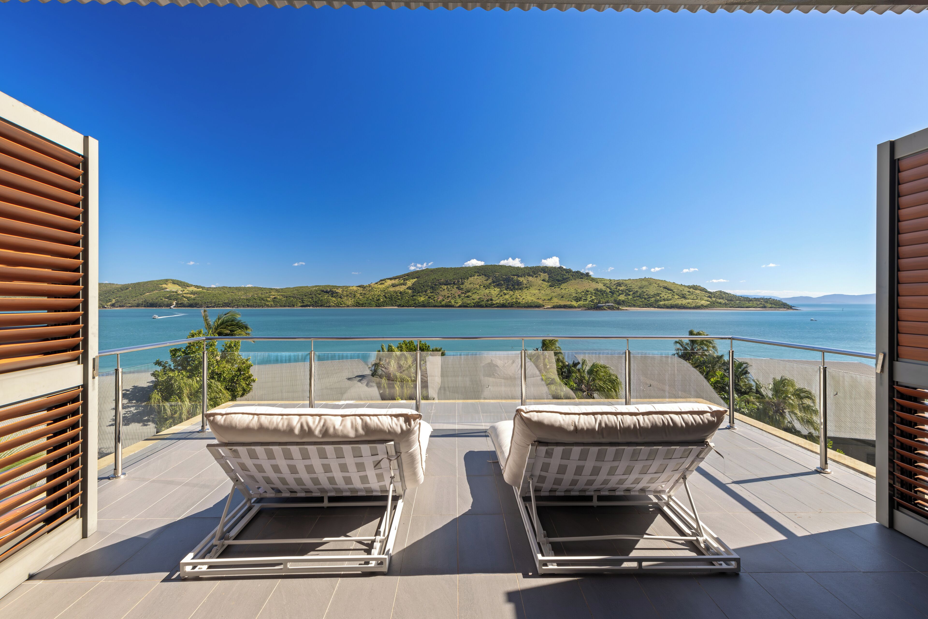 Un balcon avec deux fauteuils blancs, une vue dégagée sur la mer et un paysage vallonné en arrière-plan.