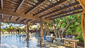 An outdoor patio with a grill, seating, and a pool area.