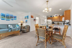 A modern living room with a sofa, armchair, and dining table with chairs. There is a kitchen area with cabinets and a countertop. - Garden oasis, spacious lanai & open concept living (Kihei)