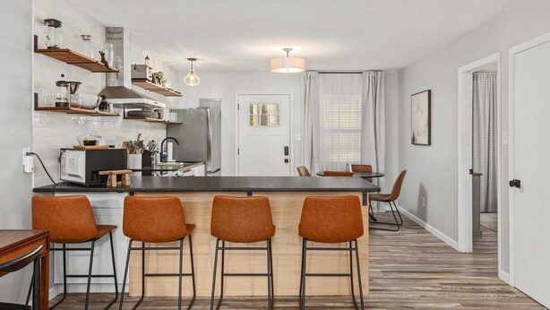 Una cocina moderna con una isla central, taburetes de bar y estantes de madera.