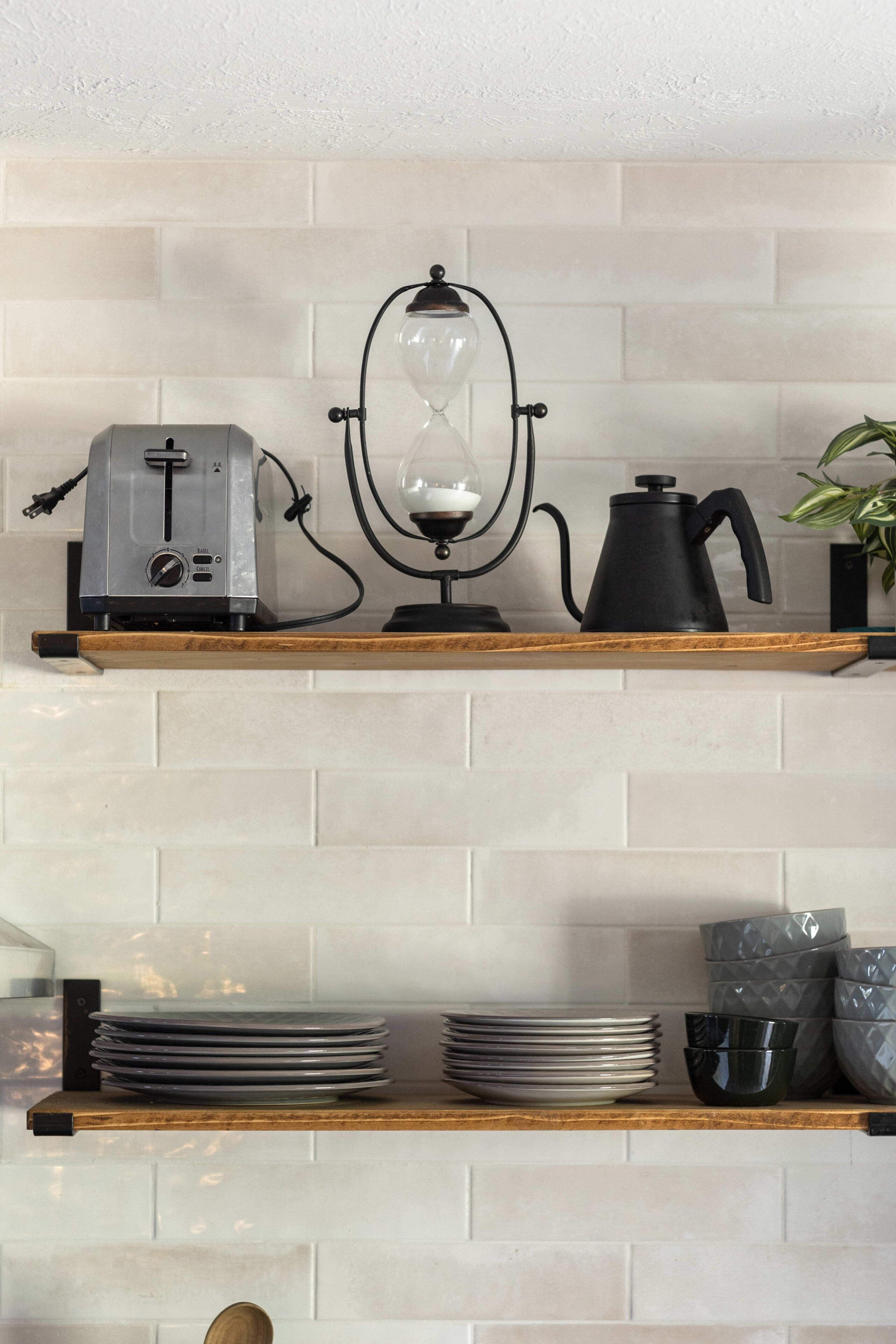 Una cocina con dos repisas de madera, un tostador, una cafetera y platos apilados.