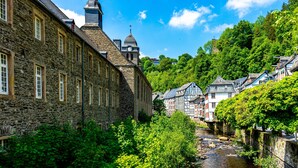 A stone building with a clock tower, a river, and lush greenery. - 1 Bedroom Apartment in Hattingen (Hattingen)