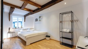 A bedroom with a bed, wooden beams, a window, a bedside table, a hanging shelf, and a radiator. - 1 Bedroom Apartment in Hattingen (Hattingen)