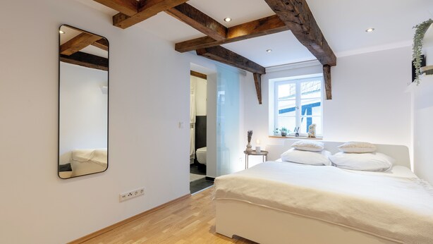 A bedroom with a large bed, wooden beams, a mirror, and a window. - 1 Bedroom Apartment in Hattingen (Hattingen)