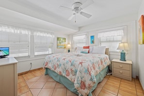 A bedroom with a bed, a desk, a nightstand, and a ceiling fan.