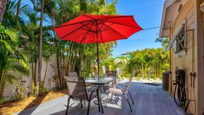 Une terrasse avec une table et des chaises, un parasol rouge et des palmiers.