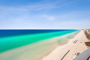 Ein Strand mit klarem türkisblauem Wasser, einem sandigen Ufer und einer Reihe von Gebäuden entlang der Küste.
