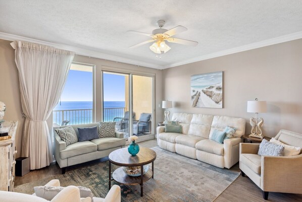 Ein großzügiges Wohnzimmer mit einem großen Fenster zum Meer, einem Deckenventilator und Blick auf den Strand.