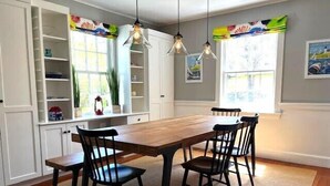 Un coin repas avec une table en bois et quatre chaises, des meubles blancs et des luminaires suspendus.