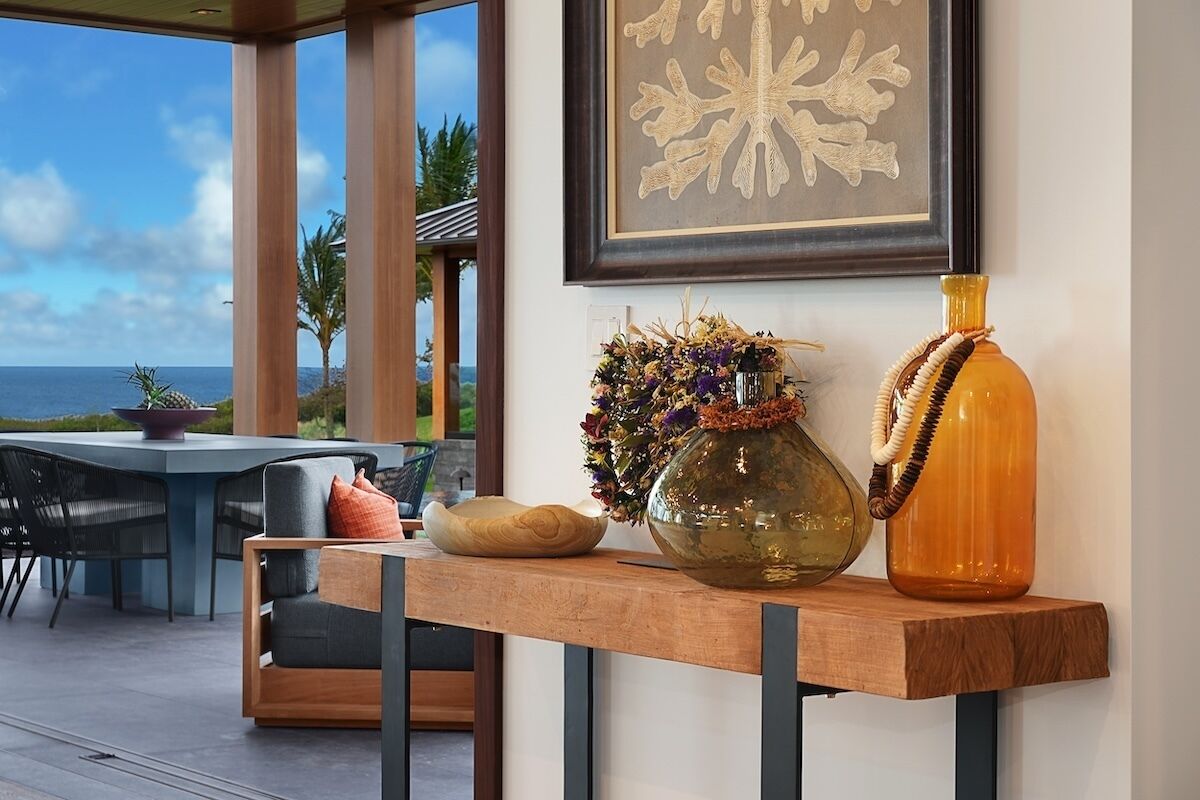 A wooden console table with decorative vases and a bowl, set against a window overlooking a scenic view.