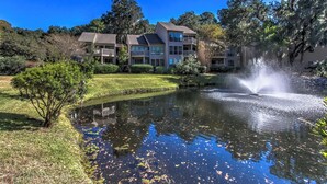 A residential area with a pond, a fountain, and multi-story buildings with balconies. - 2382 Lighthouse Tennis: 1 Bedroom Pet Friendly, Free Bikes, Pool, Tennis (Hilton Head Island)