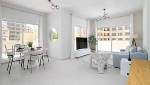 A modern living room with a dining area, large windows, and a flat-screen TV. - Nasma Holiday Homes - Bab Al Bahr Residences (Ras Al Khaimah)
