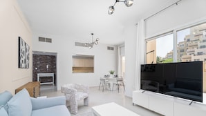 A modern living room with a sofa, a coffee table, a TV, and a dining area with chairs and a table. - Nasma Holiday Homes - Bab Al Bahr Residences (Ras Al Khaimah)
