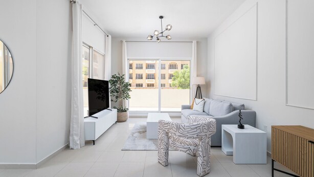 A modern living room with a flat-screen TV, a grey sofa, a patterned coffee table, and a wooden cabinet. - Nasma Holiday Homes - Bab Al Bahr Residences (Ras Al Khaimah)