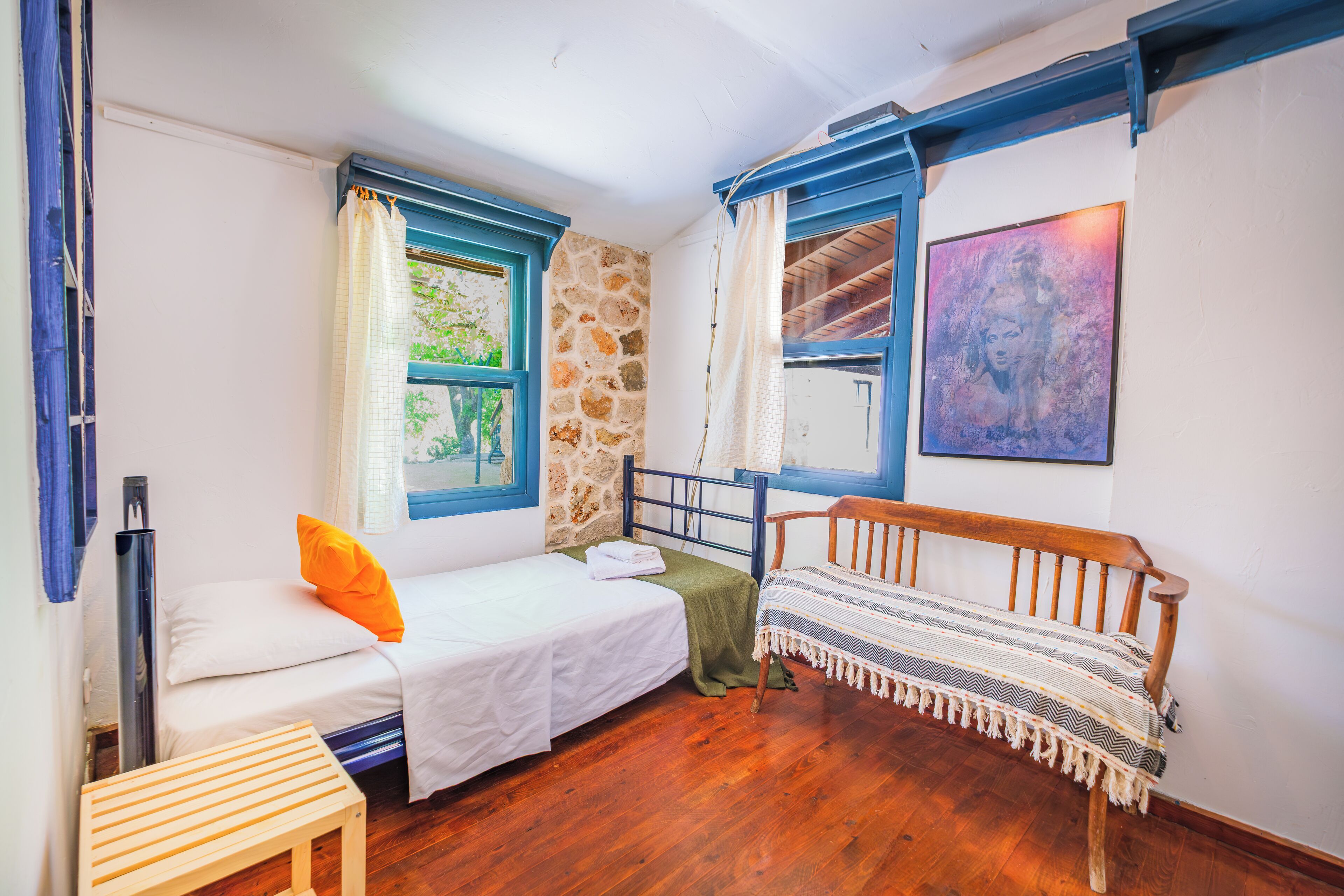 Una habitación pequeña y acogedora con cama, un banco y una ventana con cortinas.