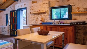 Una cucina rustica con parete in pietra, mobili in legno, un tavolo bianco e una finestra vista verde.