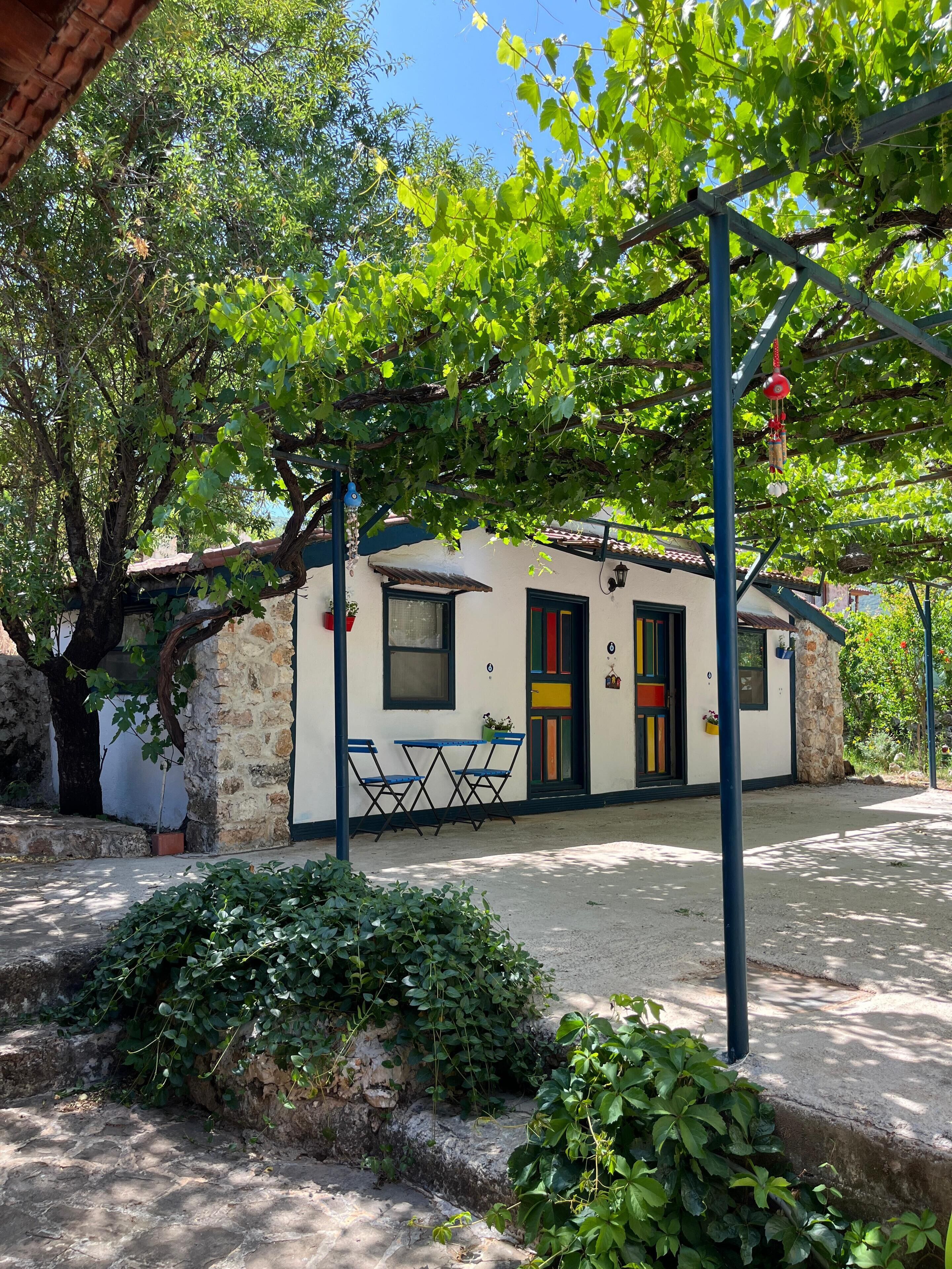 A rustic building with a stone facade, a tiled roof, and a small outdoor seating area with blue chairs.