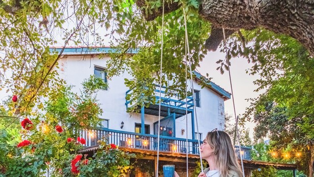 Una persona seduta su un'altalena in una zona con decking in legno, con un edificio sullo sfondo.
