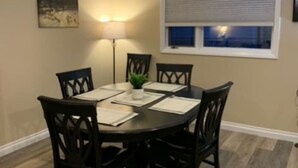 A dining area with a round table, six chairs, a small plant, and a window with blinds. - Longhorn Lodge - Extended Stay (Great Falls)