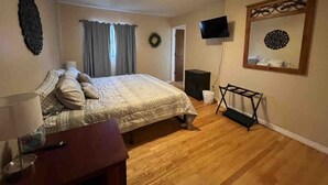 A bedroom with a bed, a TV, a wooden floor, a desk, and a chair. - Longhorn Lodge - Extended Stay (Great Falls)